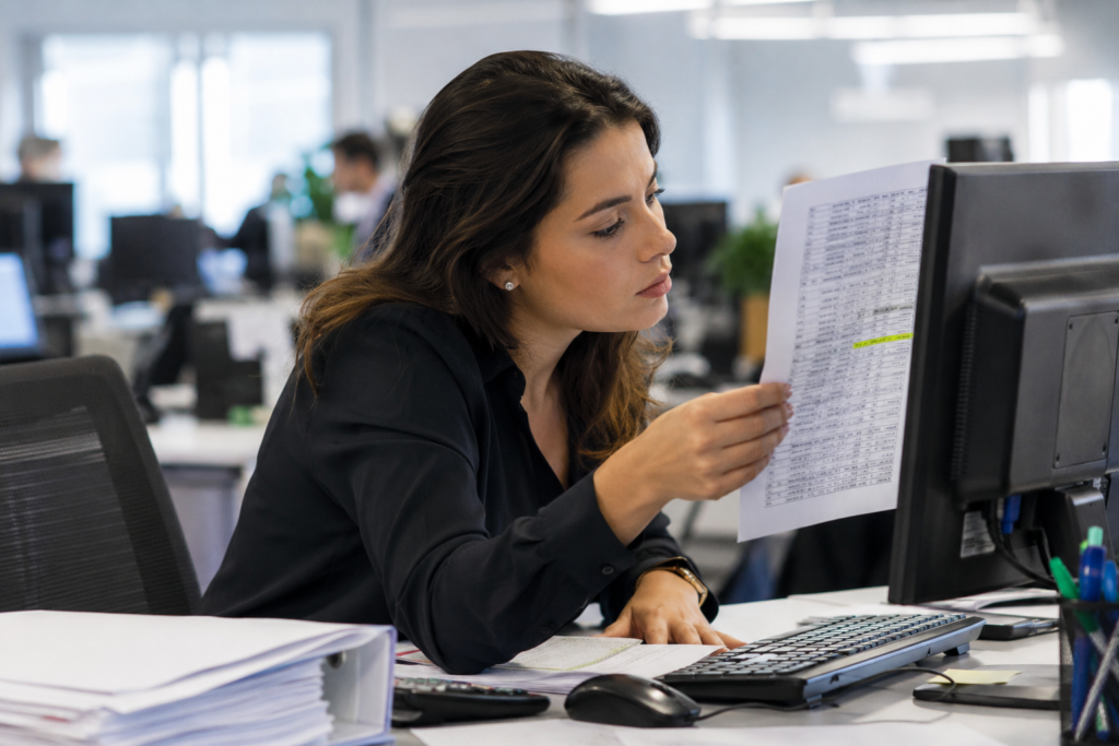 Office worker comparing a printed figure against on-screen data to verify a statistic
